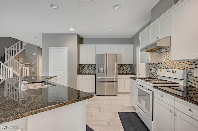 kitchen with sink, stainless steel fridge, gas range gas stove, white cabinetry, and dark stone countertops