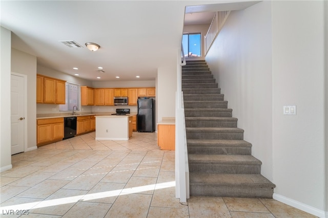 kitchen with a kitchen island, light brown cabinetry, sink, light tile patterned floors, and black appliances