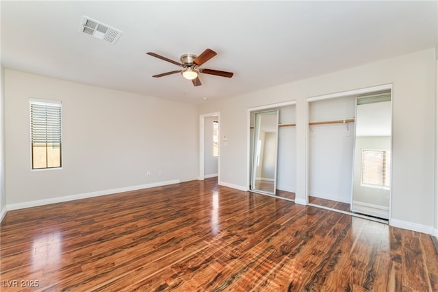 unfurnished bedroom featuring dark wood-type flooring, ceiling fan, and two closets