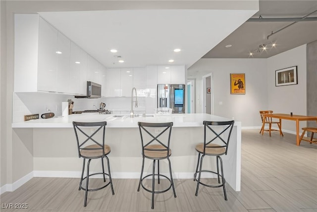 kitchen featuring sink, a breakfast bar, appliances with stainless steel finishes, white cabinets, and kitchen peninsula