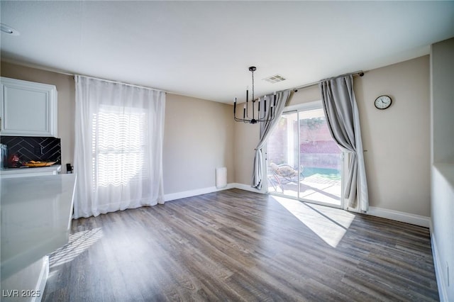 unfurnished dining area with an inviting chandelier and dark hardwood / wood-style flooring