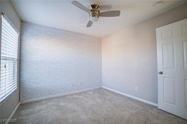 carpeted spare room with ceiling fan and brick wall