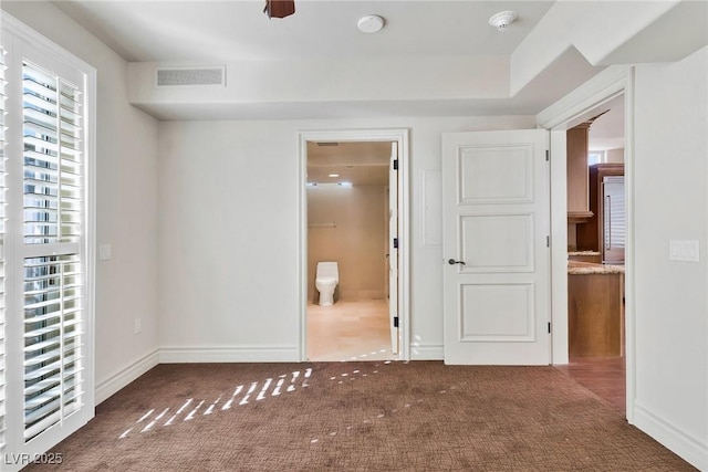 unfurnished bedroom with ensuite bath and dark colored carpet