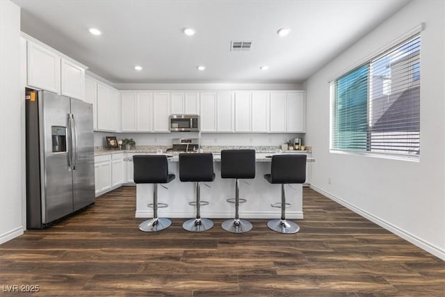 kitchen with white cabinetry, appliances with stainless steel finishes, dark hardwood / wood-style flooring, and a kitchen island with sink