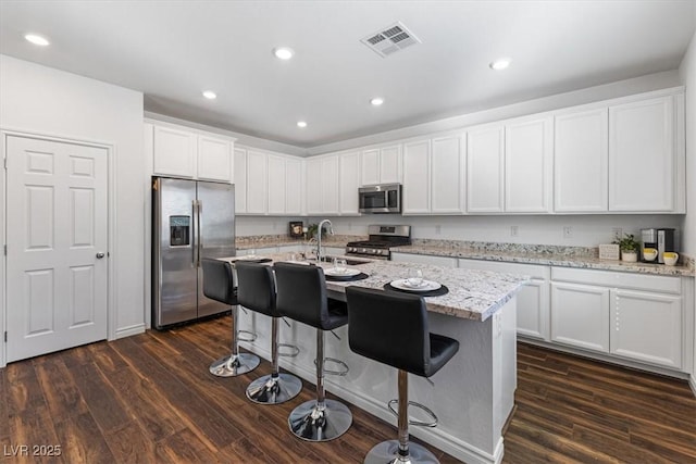 kitchen featuring appliances with stainless steel finishes, light stone countertops, and a center island with sink