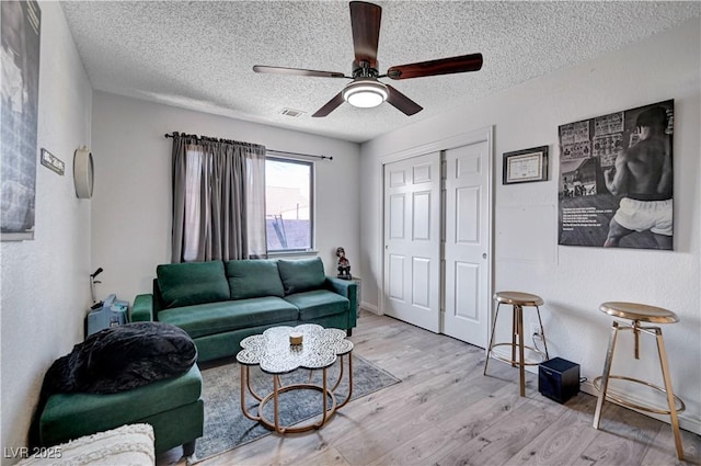 living room featuring ceiling fan, light hardwood / wood-style floors, and a textured ceiling