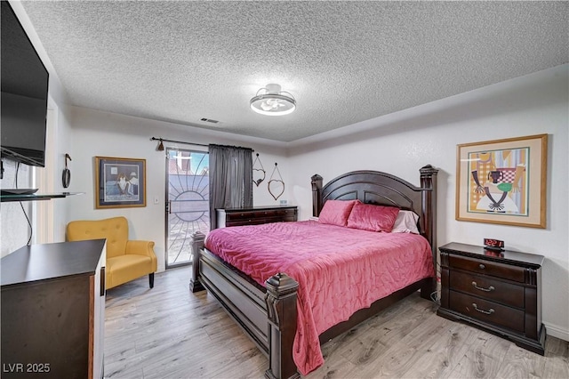 bedroom featuring access to exterior, a textured ceiling, and light wood-type flooring