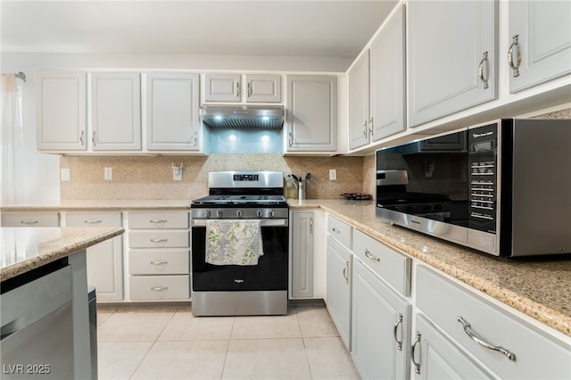 kitchen with appliances with stainless steel finishes, light tile patterned floors, white cabinets, and backsplash