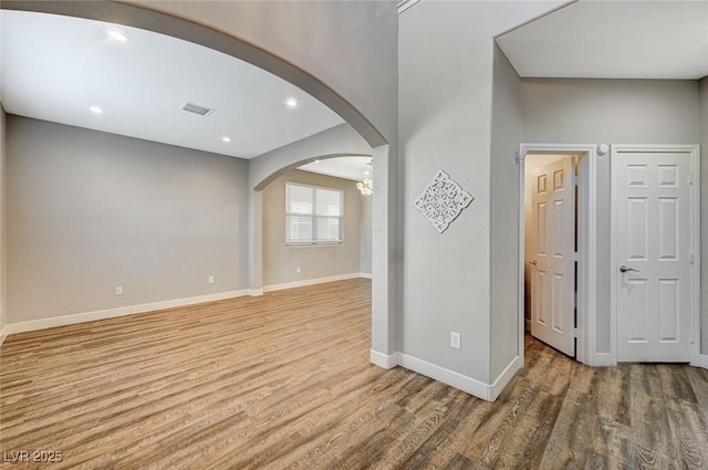 spare room featuring visible vents, arched walkways, baseboards, light wood-type flooring, and recessed lighting