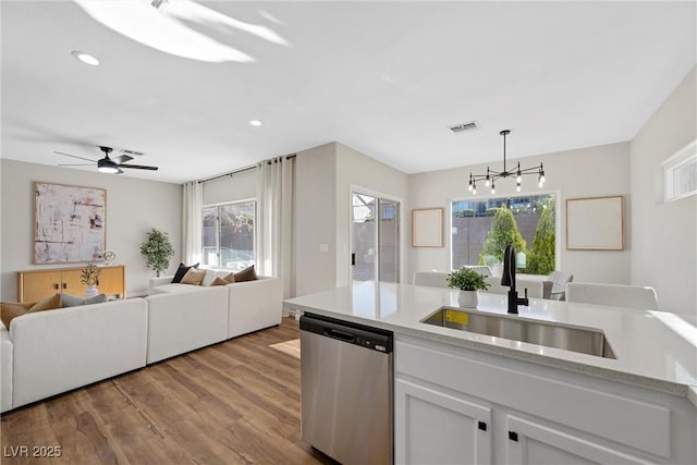 kitchen featuring sink, dishwasher, white cabinets, decorative light fixtures, and light wood-type flooring