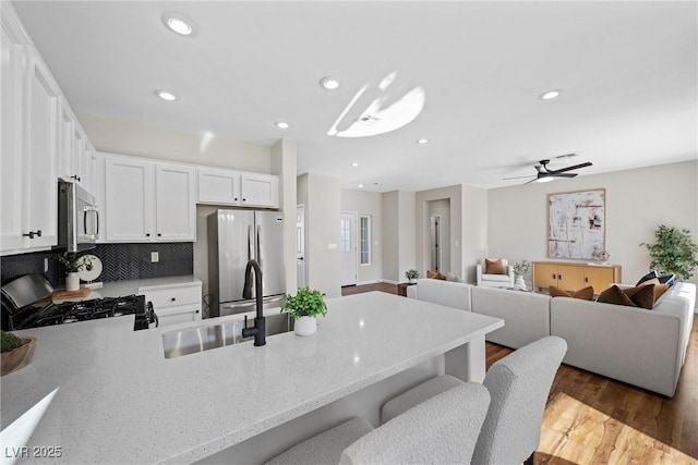 kitchen featuring a breakfast bar area, tasteful backsplash, hardwood / wood-style flooring, stainless steel appliances, and white cabinets