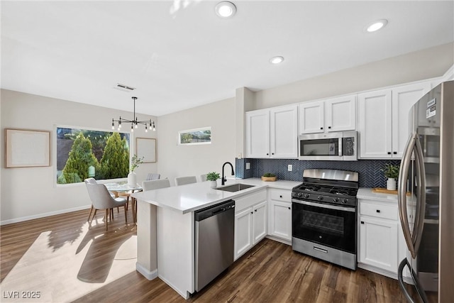 kitchen with sink, appliances with stainless steel finishes, white cabinetry, decorative light fixtures, and kitchen peninsula