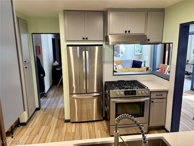 kitchen featuring stainless steel appliances, gray cabinets, light countertops, and under cabinet range hood