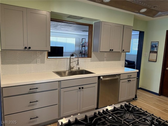 kitchen with stainless steel dishwasher, gray cabinets, light countertops, and a sink