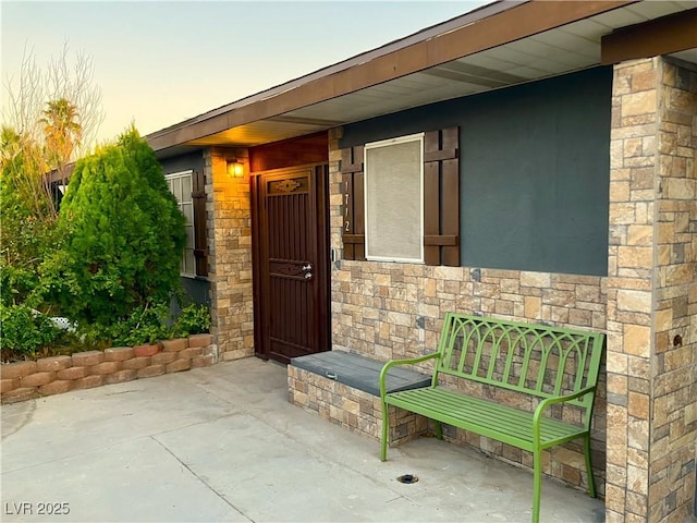 exterior entry at dusk featuring stone siding and a patio area