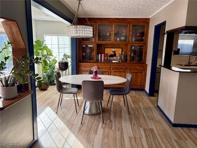 dining area with a textured ceiling, ornamental molding, baseboards, and light wood-style floors