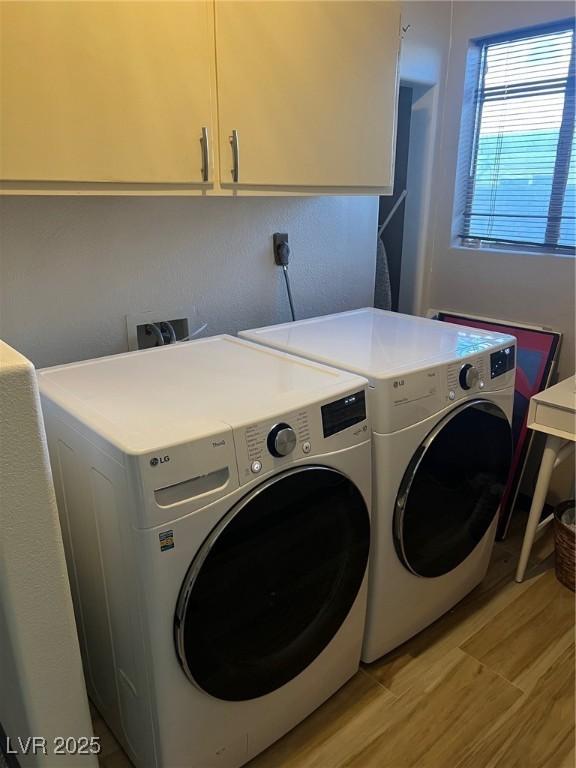 clothes washing area featuring separate washer and dryer, light hardwood / wood-style floors, and cabinets