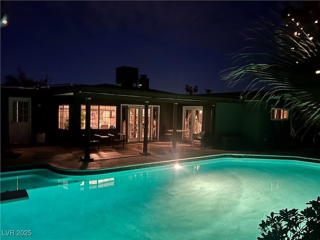 pool at twilight featuring a patio area, an outdoor pool, and french doors