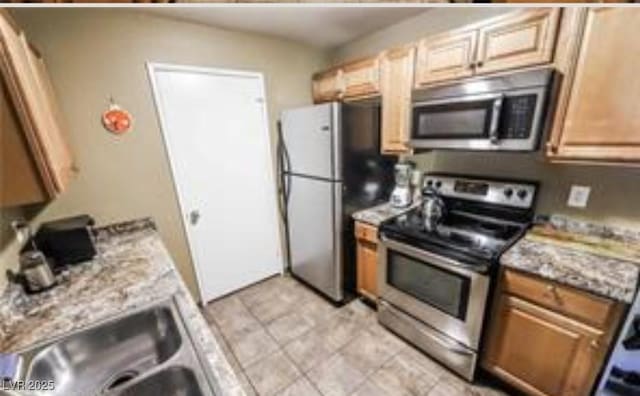 kitchen featuring stainless steel appliances, light stone countertops, and sink