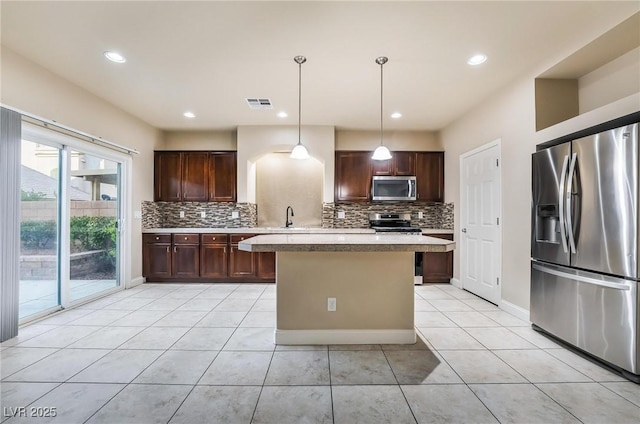 kitchen with pendant lighting, dark brown cabinets, stainless steel appliances, a kitchen island, and decorative backsplash