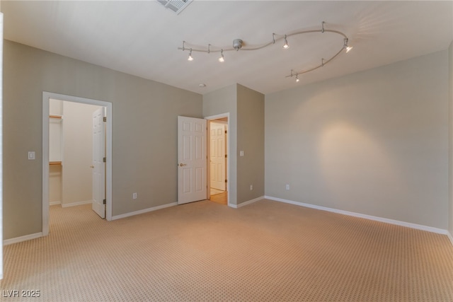 unfurnished bedroom featuring rail lighting, a spacious closet, and light colored carpet