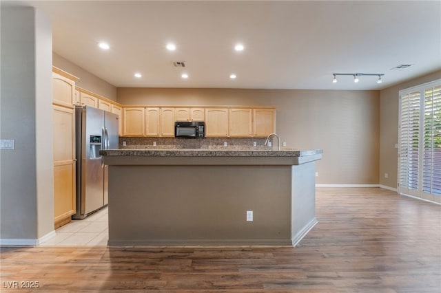 kitchen featuring sink, stainless steel fridge, an island with sink, decorative backsplash, and light wood-type flooring