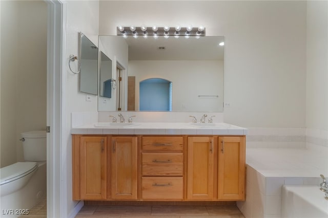 bathroom featuring vanity, toilet, and tiled bath