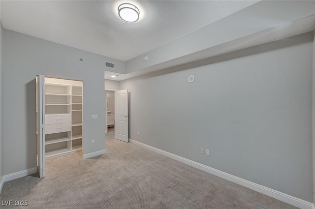 unfurnished bedroom with a walk in closet, visible vents, light carpet, and baseboards