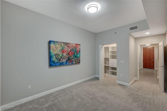 unfurnished bedroom with a walk in closet, a closet, light colored carpet, visible vents, and baseboards