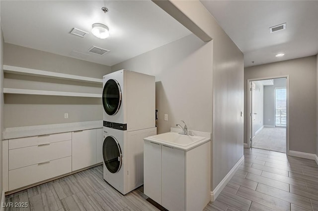 laundry area with visible vents, cabinet space, a sink, and stacked washer and clothes dryer