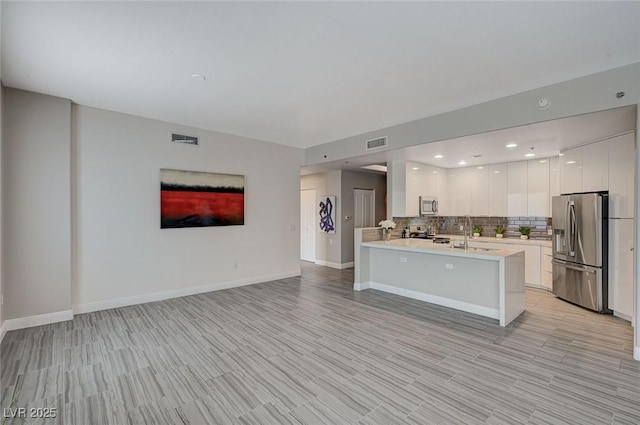 kitchen with light countertops, appliances with stainless steel finishes, open floor plan, white cabinets, and a peninsula