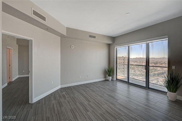 empty room with baseboards, visible vents, and dark wood-style flooring