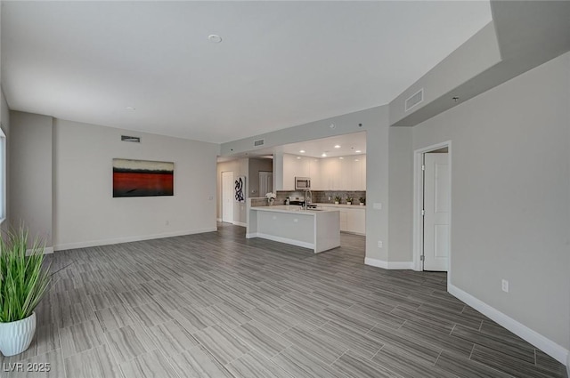 unfurnished living room with light wood finished floors, visible vents, and baseboards