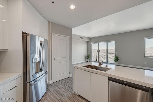 kitchen with appliances with stainless steel finishes, white cabinets, light countertops, and a sink