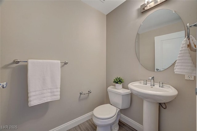 half bath with toilet, baseboards, and wood finished floors