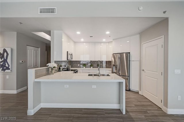 kitchen with stainless steel appliances, a peninsula, a sink, visible vents, and light countertops