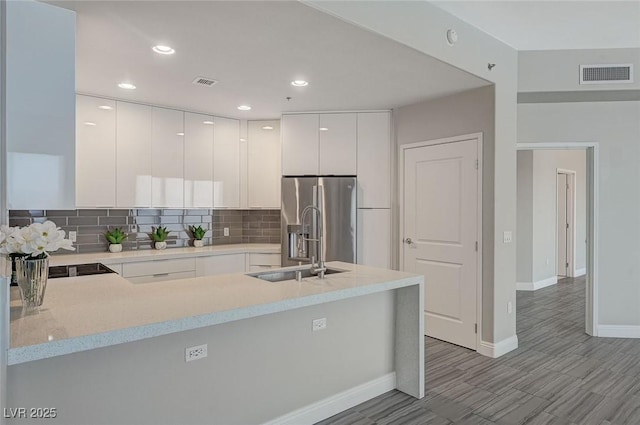 kitchen with a peninsula, visible vents, white cabinets, stainless steel fridge with ice dispenser, and modern cabinets