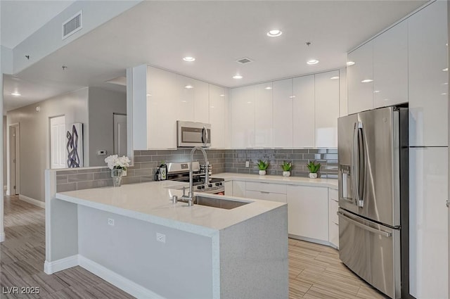 kitchen featuring a peninsula, appliances with stainless steel finishes, light countertops, and white cabinetry