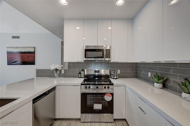 kitchen featuring modern cabinets, visible vents, appliances with stainless steel finishes, white cabinetry, and light stone countertops