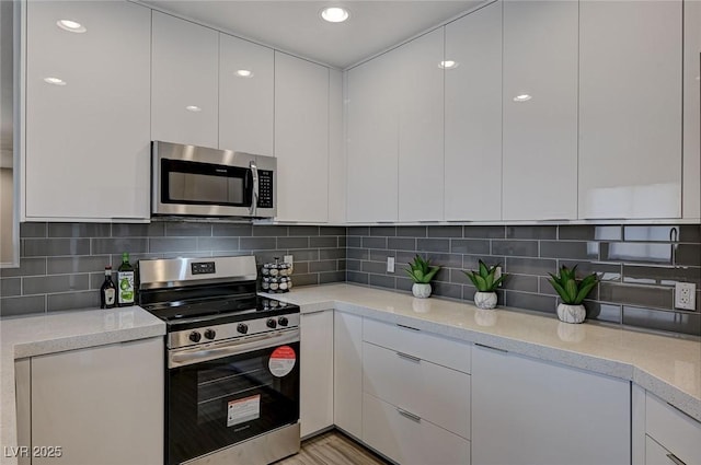 kitchen with light stone counters, stainless steel appliances, white cabinetry, decorative backsplash, and modern cabinets