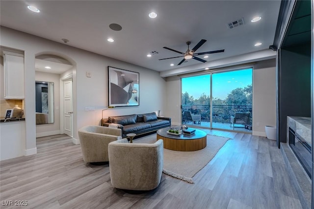 living area featuring light wood-type flooring, visible vents, arched walkways, and recessed lighting