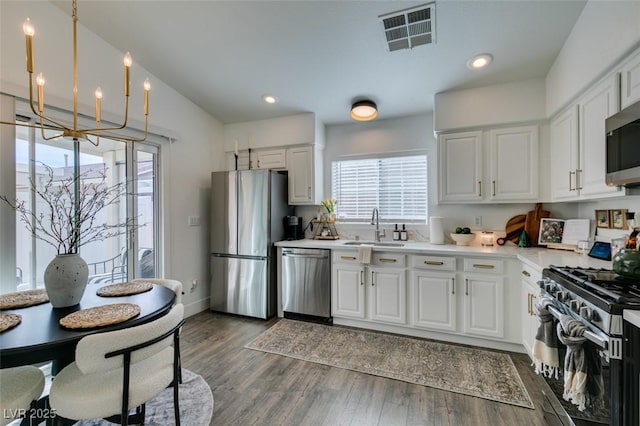 kitchen featuring dark wood-type flooring, sink, white cabinetry, decorative light fixtures, and appliances with stainless steel finishes