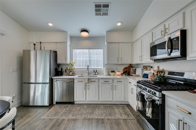 kitchen with stainless steel appliances, white cabinetry, wood-type flooring, and sink