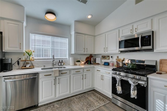 kitchen with appliances with stainless steel finishes, dark hardwood / wood-style flooring, sink, and white cabinets