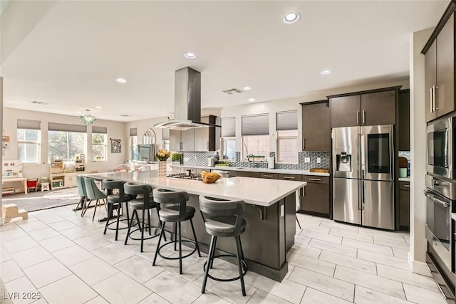 kitchen with a breakfast bar, tasteful backsplash, island range hood, a center island, and stainless steel appliances