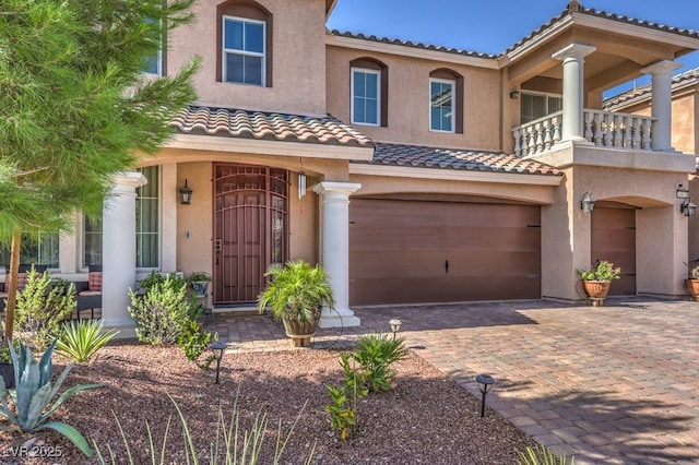 mediterranean / spanish-style home featuring stucco siding, a tile roof, decorative driveway, and a garage