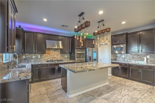 kitchen with light stone counters, under cabinet range hood, a sink, visible vents, and appliances with stainless steel finishes