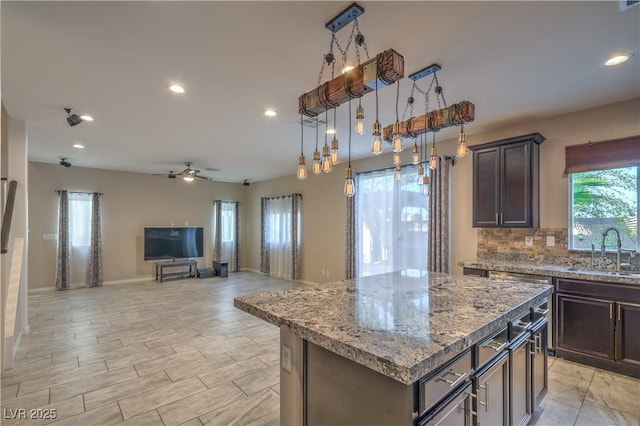 kitchen with recessed lighting, decorative backsplash, a kitchen island, a sink, and light stone countertops