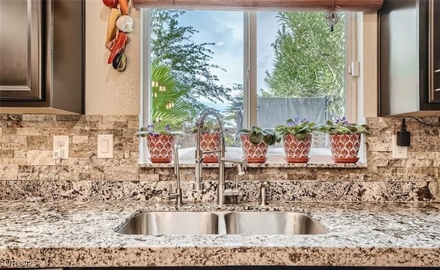 kitchen with dark brown cabinetry, light stone countertops, and a sink