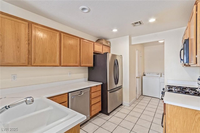 kitchen with appliances with stainless steel finishes, washer and clothes dryer, sink, and light tile patterned floors